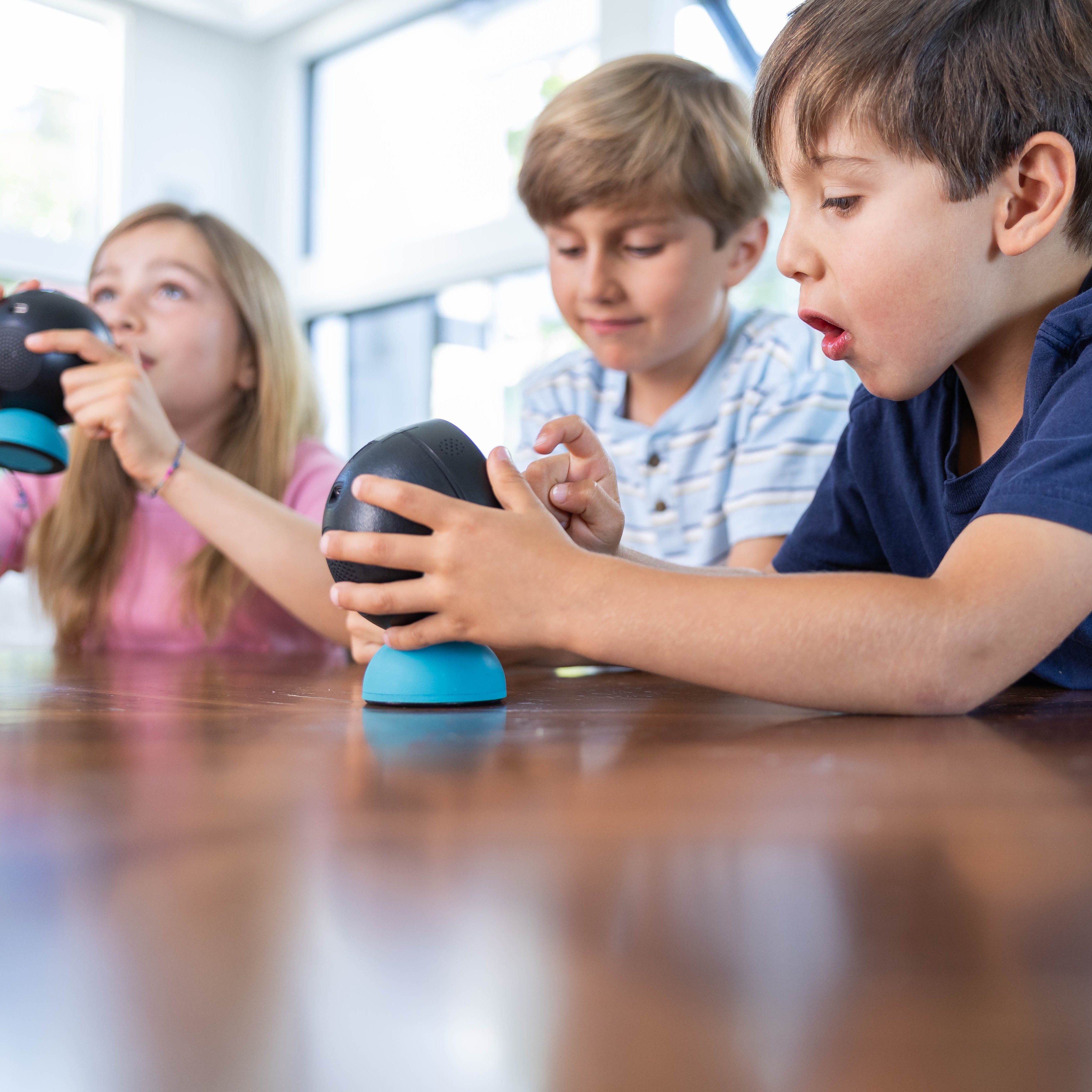 Three children playing with devices on a table.